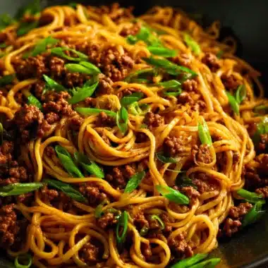 Mongolian ground beef noodles served in a bowl with vegetables and garnishes.