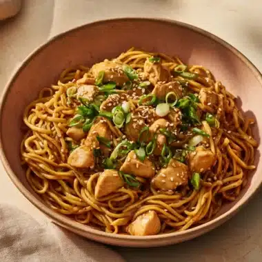 Plate of sticky garlic chicken noodles garnished with parsley.