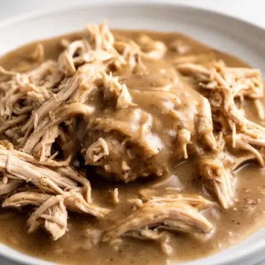 Crockpot chicken and gravy served on a plate with mashed potatoes