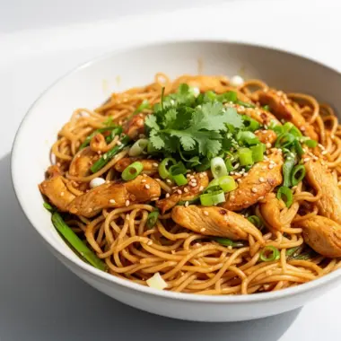 Plate of sticky garlic chicken noodles garnished with herbs and vegetables.